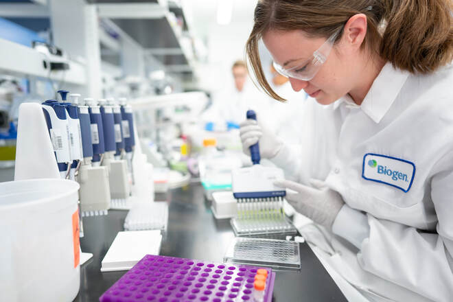 A scientist wearing safety goggles and a lab coat labeled "Biogen" in a lab