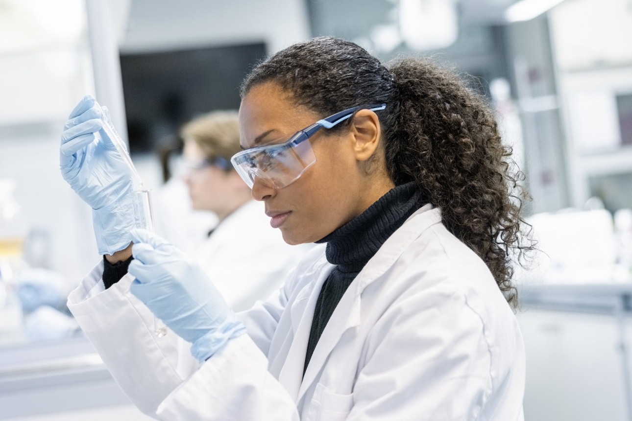 Woman scientist conducting an experiment in a laboratory. Female lab technician wearing lab coat, protective eyewear and gloves working in a chemistry lab.